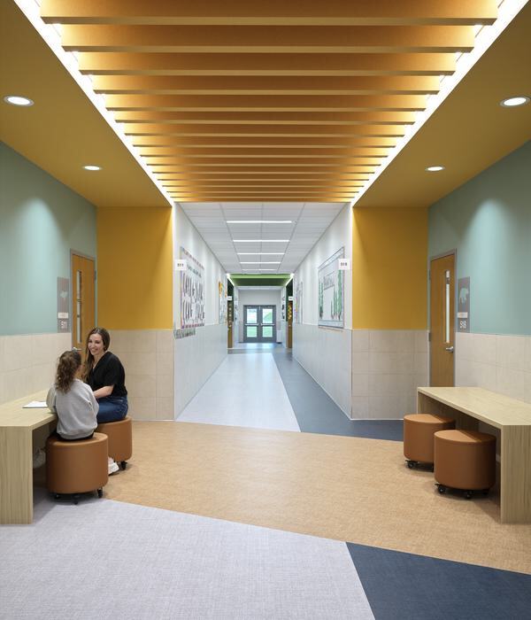 A bright hallway features a mix of colors, modern seating, and artwork on the walls, with two people engaged in conversation at a table.