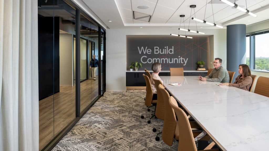 A modern conference room features a large table, contemporary decor, and a slogan on the wall about building community.