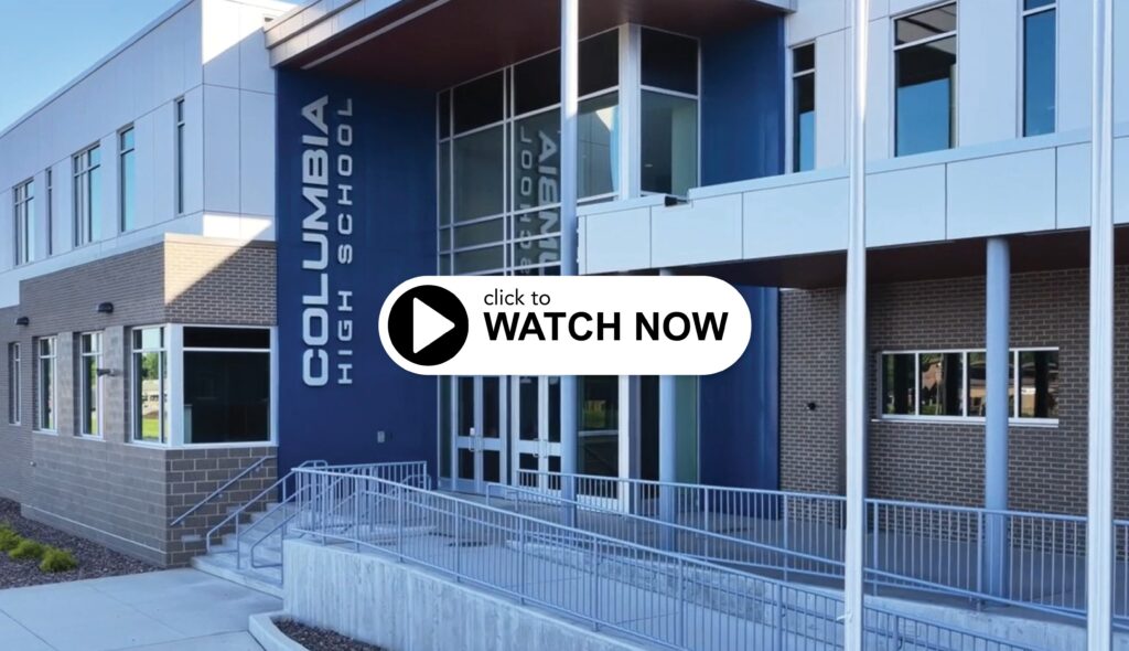 A modern school building with large windows and a prominent entrance featuring the name "Columbia High School." A play button encourages viewing.
