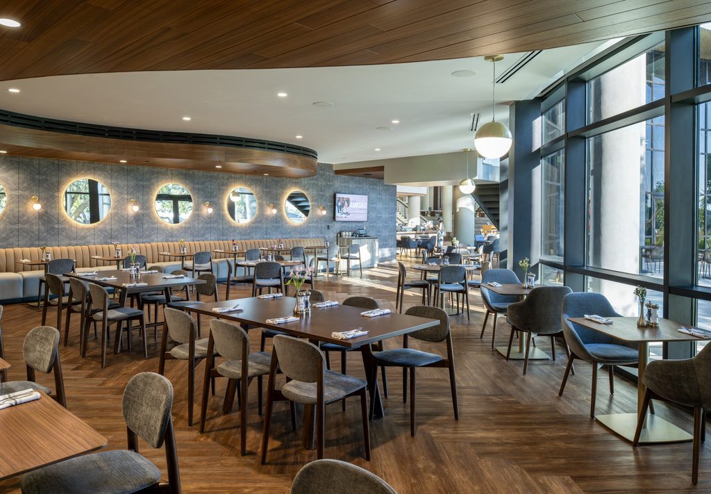 New cafe/restaurant spsace features curved walls and curved exterior floor-to-ceiling windows, accented by rich browns and medium greys for a modern, cozy feel.