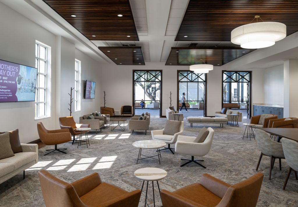 Contemporary church gathering space featuring comfortable seating arrangements, wood-paneled ceilings, pendant lighting and large windows that fill the room with natural light.
