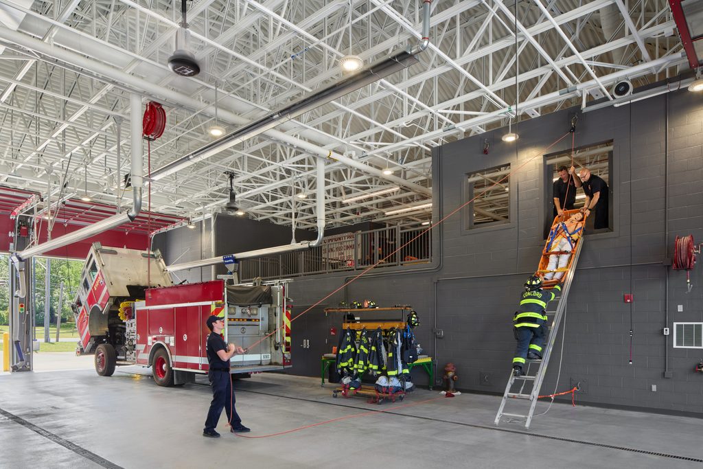 Mezzanine training in a fire station bay with active training in progress using a pulley system and ladder to lift or lower a dummy person.